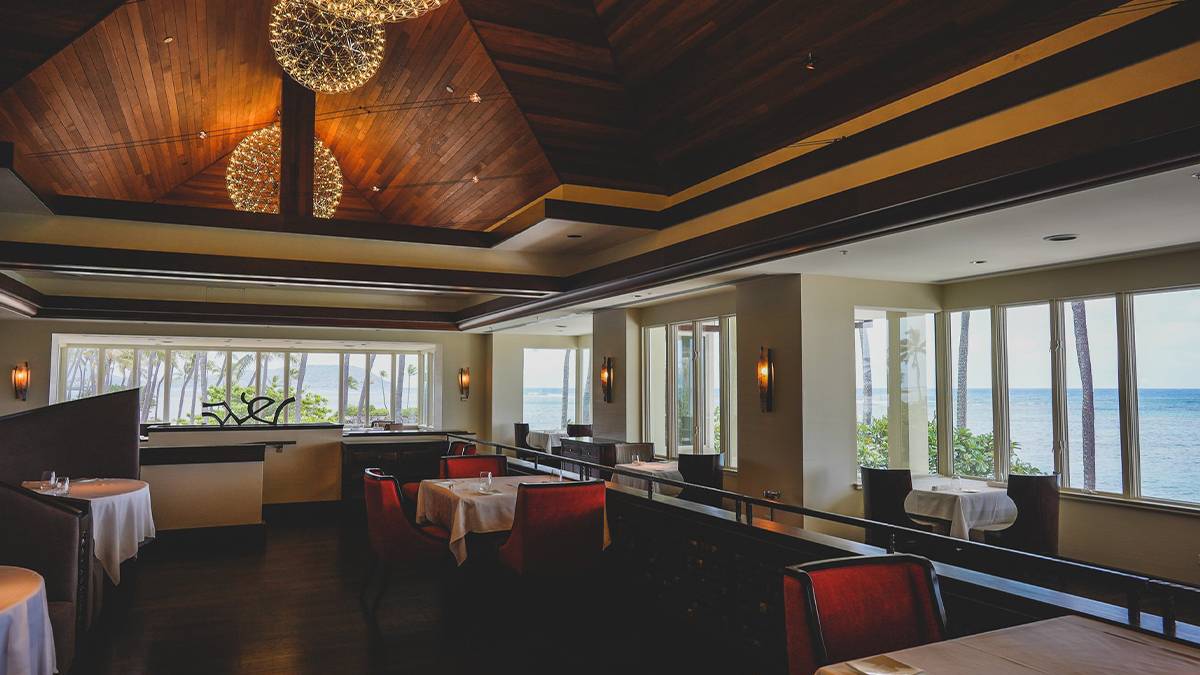 View of a low lit dining room with red chairs and a wooden ceiling at Hoku's in Oahu, Hawaii, USA